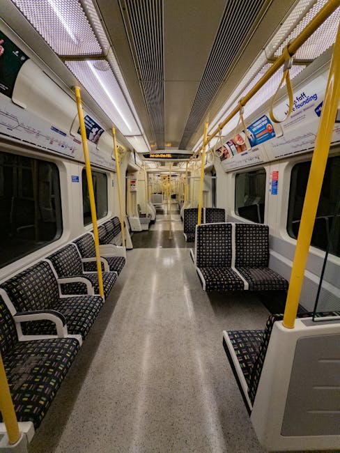 Interior view of the carriage on a commuter train at Seven Sisters station, showing clean, well-maintained seating areas with upholstered benches featuring dark patterned fabric. The aisle has a smoot